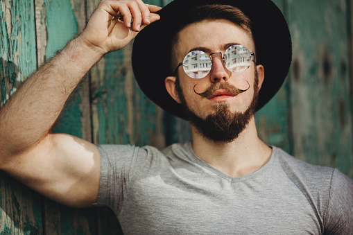 Fashion portrait of young bearded hipster man in sunglasses and hat with fashionable mustaches. People, emotions, barbershop and style concept