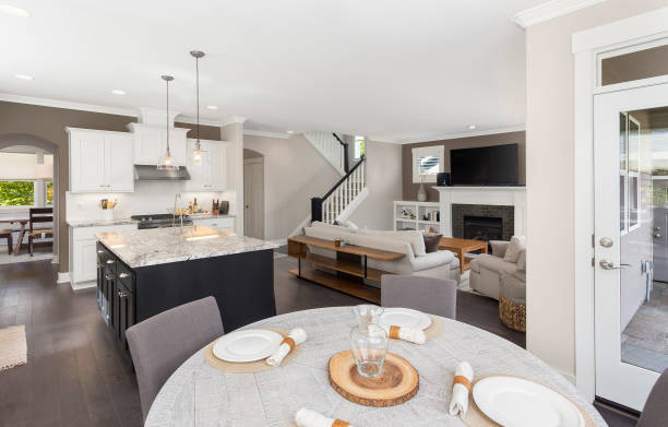 panorama of beautiful kitchen, living room, and eating nook in new luxury home with island, pendant lights, stainless steel appliances, and hardwood floors - living room showcase interior luxury dining room imagens e fotografias de stock