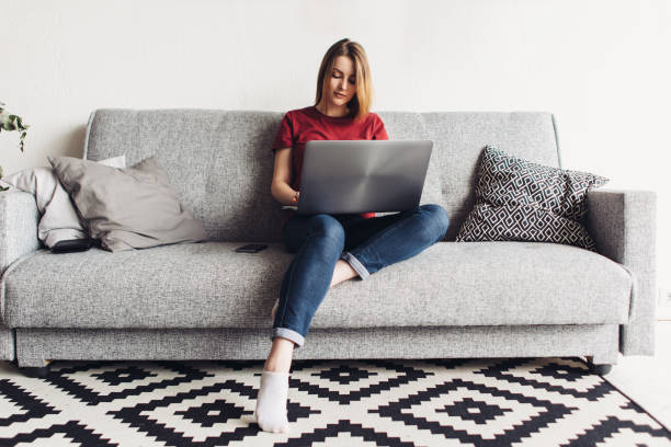 istock Woman using laptop computer sitting on sofa in living room 972785456