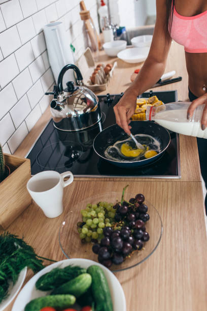 istock Fitness woman prepare omlette at the kitchen. Mixing milk and eggs into frying pan. 972785708