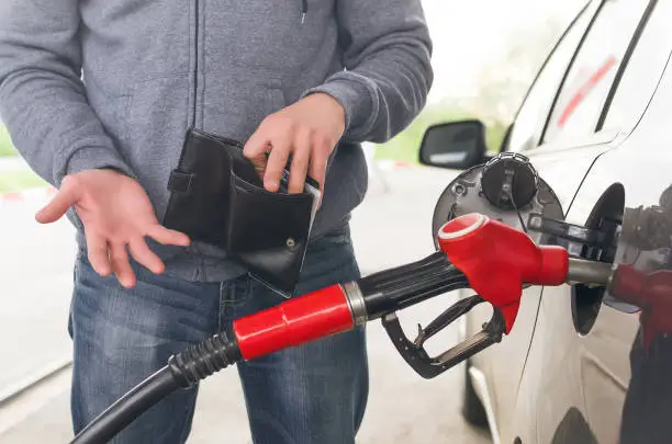 Lack of money for gasoline and fuel. Expensive gasoline. Driver man holds one dollar end empty wallet against the background of a fuel nozzle in the gas tank. increase in gasoline prices concept.