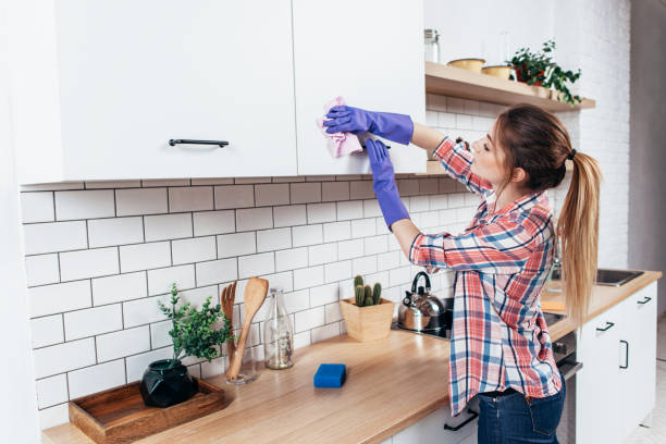 Woman in gloves cleaning cabinet with rag at home kitchen. stock photo