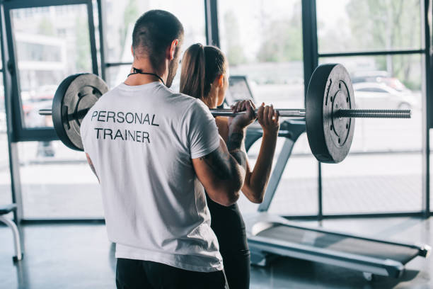 male personal trainer helping sportswoman to do exercises with barbell at gym male personal trainer helping sportswoman to do exercises with barbell at gym fitness instructor stock pictures, royalty-free photos & images