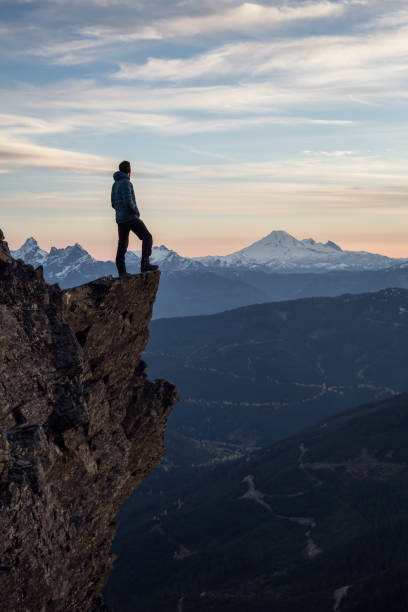 Man on top of a Cliff Adventurous man is standing on top of the mountain and enjoying the beautiful view during a vibrant sunset. Taken on top of Cheam Peak in Chilliwack, East of Vancouver, BC, Canada. pacific northwest region stock pictures, royalty-free photos & images