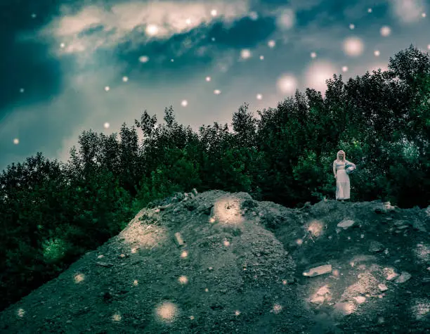 Fantasy landscape with a girl in white on a rock at twilight surrounded by magical glowing ethereal lights with forest backdrop