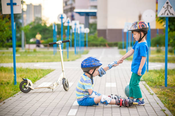 istock two boys in park, help boy with roller skates to stand up 972852748