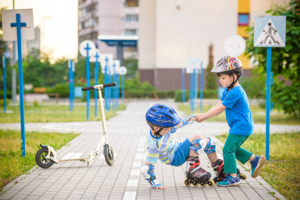 istock two boys in park, help boy with roller skates to stand up 972852766