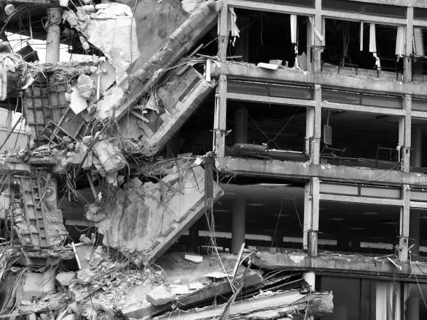 monochrome image of a demolition site of a collapsing destroyed large concrete building with smashed ruined floors and exposed interior