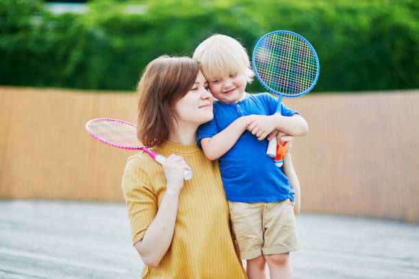 маленький мальчик играет в бадминтон с мамой на детской площадке - racquette стоковые фото и изображения
