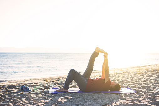 Senior woman at the beach laying on yoga mat, exercising