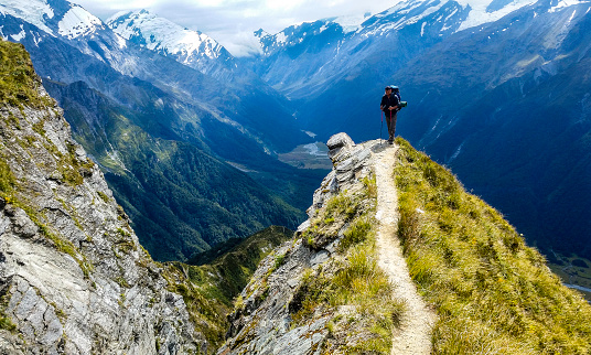 traveler at the edge of a cliff with amazing view behind him.Cascade Saddle, Mount Aspiring National Park, New Zealand