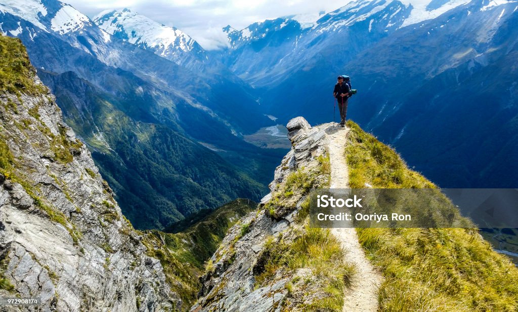 traveler at the edge of a cliff with amazing view behind him traveler at the edge of a cliff with amazing view behind him.Cascade Saddle, Mount Aspiring National Park, New Zealand New Zealand Stock Photo