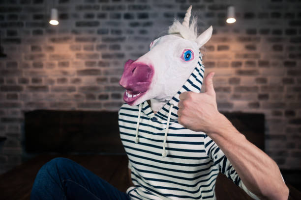 Freaky young man in comical mask sits on bed