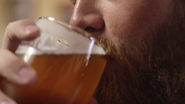 A Smiling Young White Man with a Red Beard Drinks a Beer