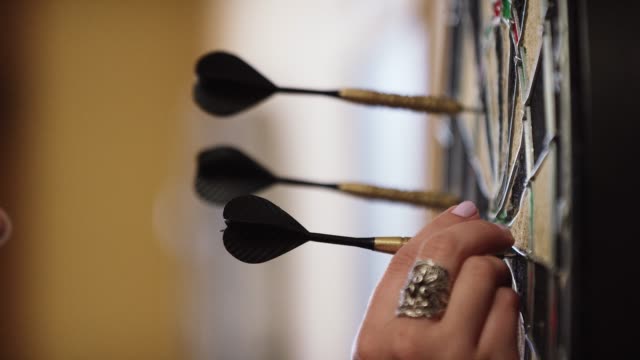 A Woman with a Ring and Pink Fingernail Polish Pulls Darts Out of a Dartboard