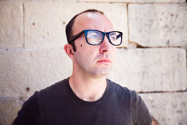 Close up portrait of a young man wearing thick black glasses and looking away.