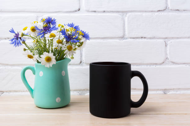 istock Black coffee mug mockup with cornflower and daisy in pitcher 973008656