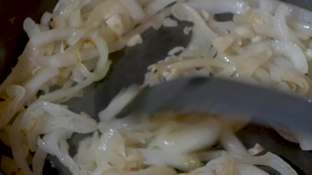 Hand stirring sliced onions and chopped garlic sauteing in a frying pan