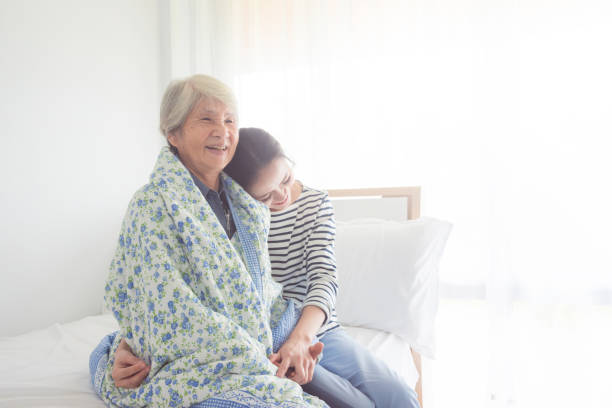 daughter hugging her senior mother at home - senior adult winter senior women daughter imagens e fotografias de stock