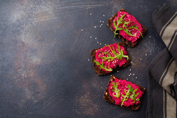 istock Bruschetta with beetroot hummus, arugula and sesame seeds on dark concrete background. Top view. 973050514