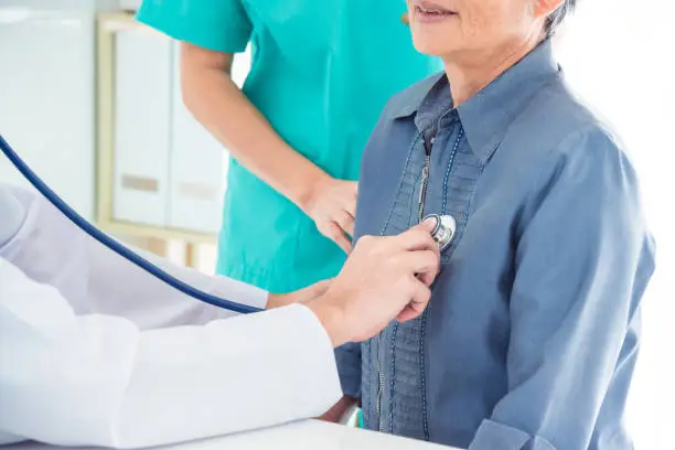 Asian doctor checking senior patient's heartbeat by stethoscope at hospital