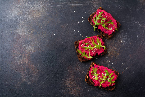 istock Bruschetta with beetroot hummus, arugula and sesame seeds on dark concrete background. Top view. 973050930