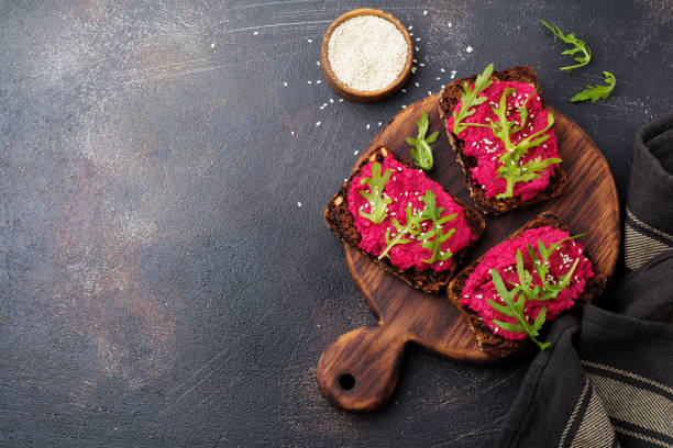 istock Bruschetta with beetroot hummus, arugula and sesame seeds on dark concrete background. Top view. 973051128