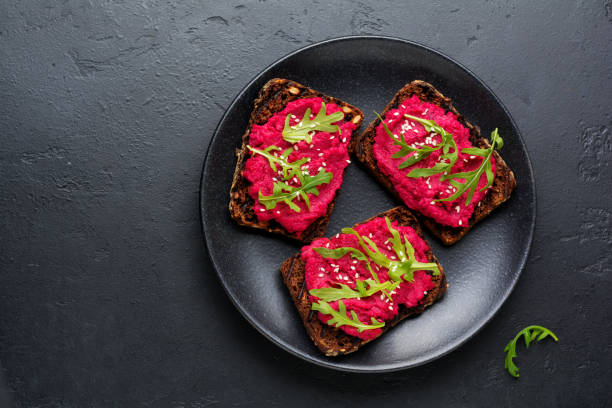 istock Bruschetta with beetroot hummus, arugula and sesame seeds on dark concrete background. Top view. 973051164