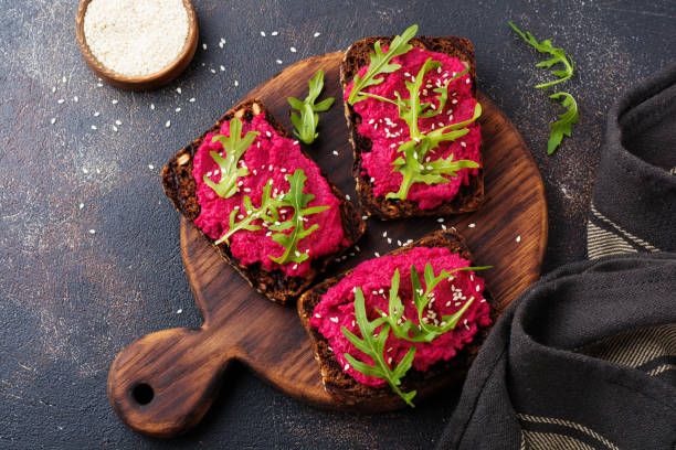 istock Bruschetta with beetroot hummus, arugula and sesame seeds on dark concrete background. Top view. 973051174