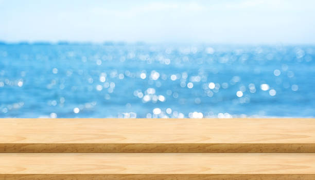 istock Empty plank wood table top with blur blue sky and sea bokeh background,Mock up template for display or montage of product or content use as banner in social media ads. 973059794
