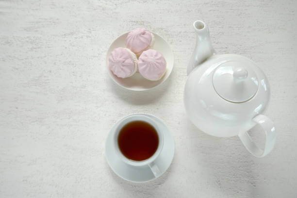 istock Morning tea flat lay. cup with tea, white teapot, pink marshmallow on a light relief background.top view, copy space 973063196