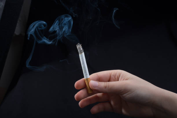 istock Hand is holding smoking cigarette on black background 973063456