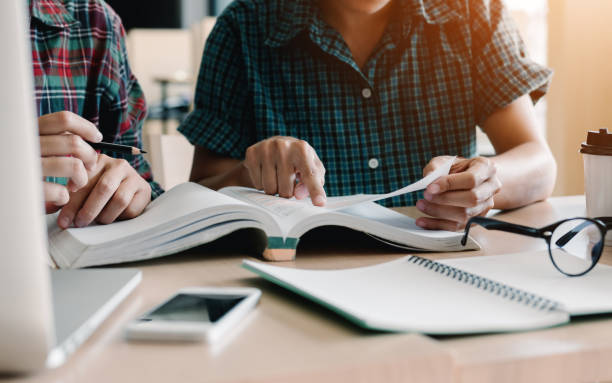 Two student reading textbook for test together in library. Two student reading textbook for test together in library. textbook stock pictures, royalty-free photos & images