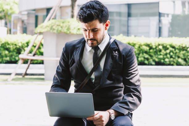 istock Handsome businessman in black elegant suit sitting and working with laptop computer on the city.Business and startup idea concept 973085232