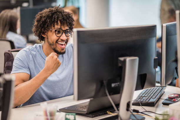 Cheerful African American programmer celebrating his success in the office.
