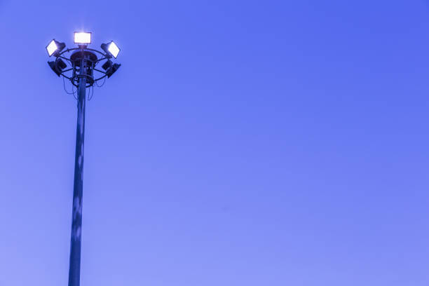 istock Spotlights tower high voltage in sport stadium on blue sky background. 973089446