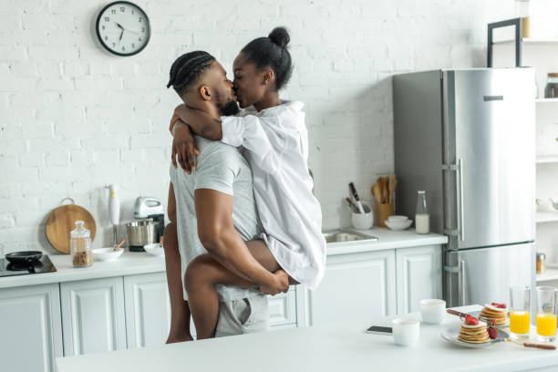 vue latérale d’afro-américains copain holding copine et ils s’embrasser dans la cuisine - african descent sex symbol couple sensuality photos et images de collection