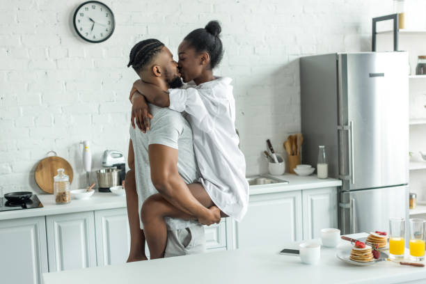 side view of african american boyfriend holding girlfriend and they kissing at kitchen - african descent sex symbol couple sensuality imagens e fotografias de stock