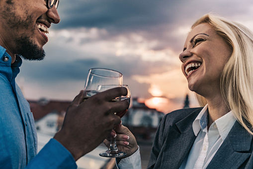 Cheerful business colleagues communicating while toasting with alcohol outdoors.