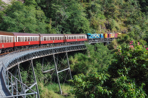 Colorful Kuranda train taking a curve on a bridge in the rainforest of Queensland, Australia.