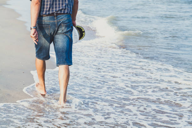 człowiek chodzi po plaży morskiej - cap embroidery blue hat zdjęcia i obrazy z banku zdjęć