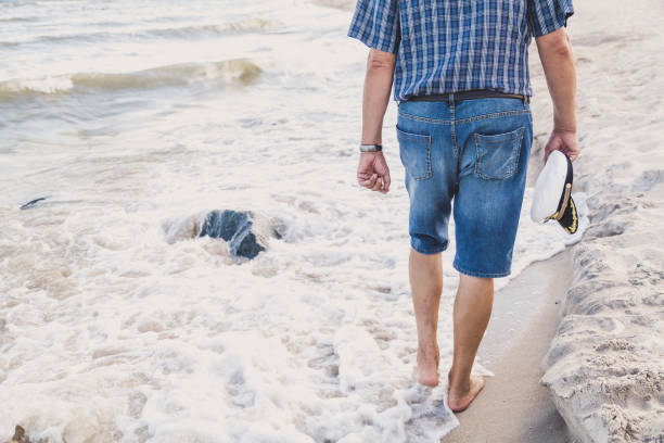 człowiek chodzi po plaży morskiej - cap embroidery blue hat zdjęcia i obrazy z banku zdjęć