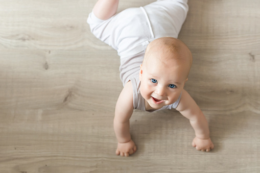 Lindo pequeño bebé acostado en madera dura y sonriente. Niño arrastrándose sobre el suelo de madera parqué y mirando hacia arriba con cara feliz. Vista desde arriba. Copyspace photo
