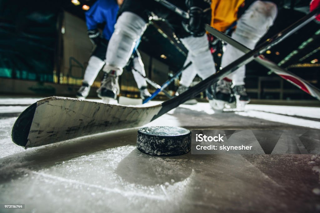 Close up of ice hockey puck and stick during a match. Close up of hockey puck and stick during a match with players in the background. Hockey Stock Photo