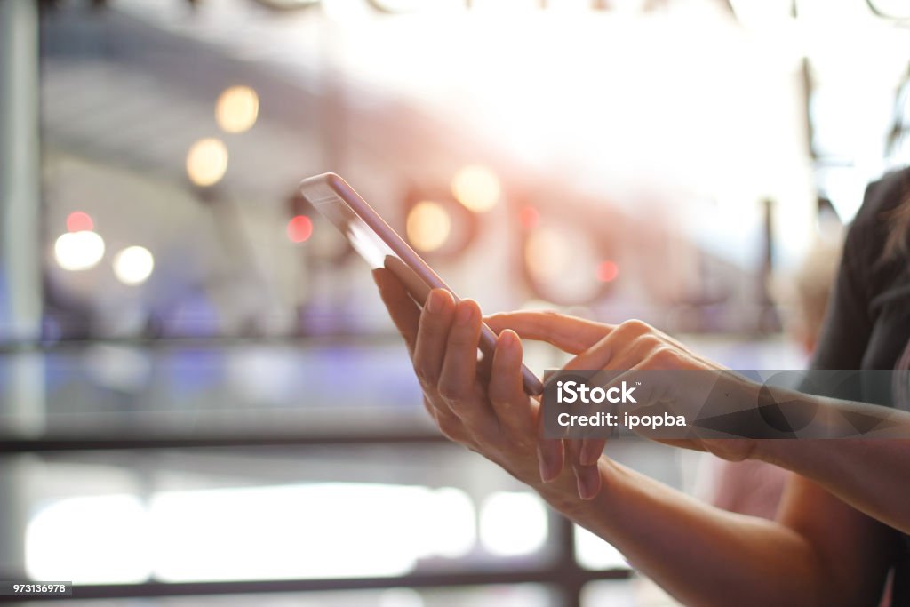 Close up of women's hands holding smartphone. Her watching sms, message, e-mail on mobile phone in coffee shop. Blurred background. Mobile Phone Stock Photo