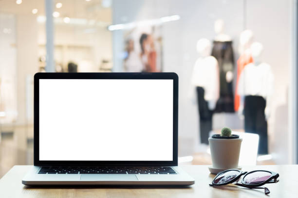 istock Laptop with blank screen on table. Clothes shop  blurred background. 973145850