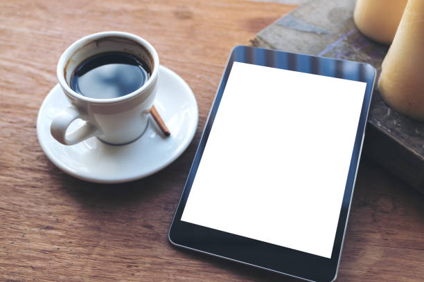 istock Top view mock up image of black tablet with white blank desktop screen and coffee cup , book , candles on vintage wooden table in cafe 973158868