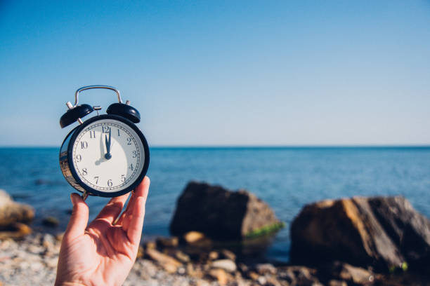 istock Hand hold watch on beach background.Alarm clock on sea and sand background different time with summer vacation.Vacation time concept. 973159088
