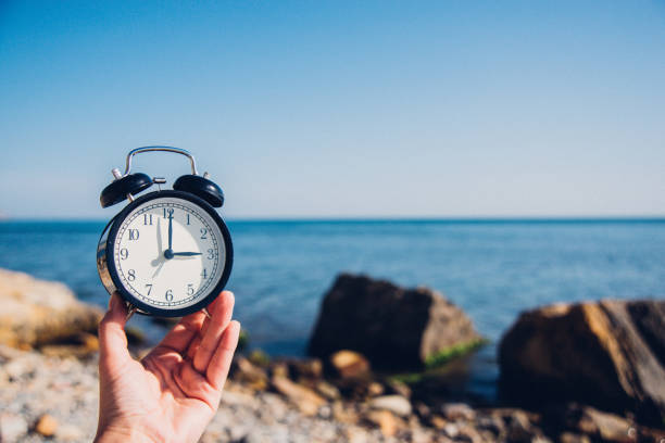 istock Hand hold watch on beach background.Alarm clock on sea and sand background different time with summer vacation.Vacation time concept. 973159282