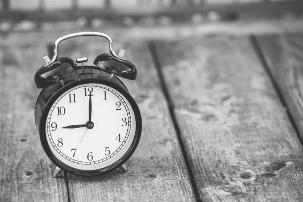 istock alarm clock showing five o'clock on wooden background, black and white image. 973159636